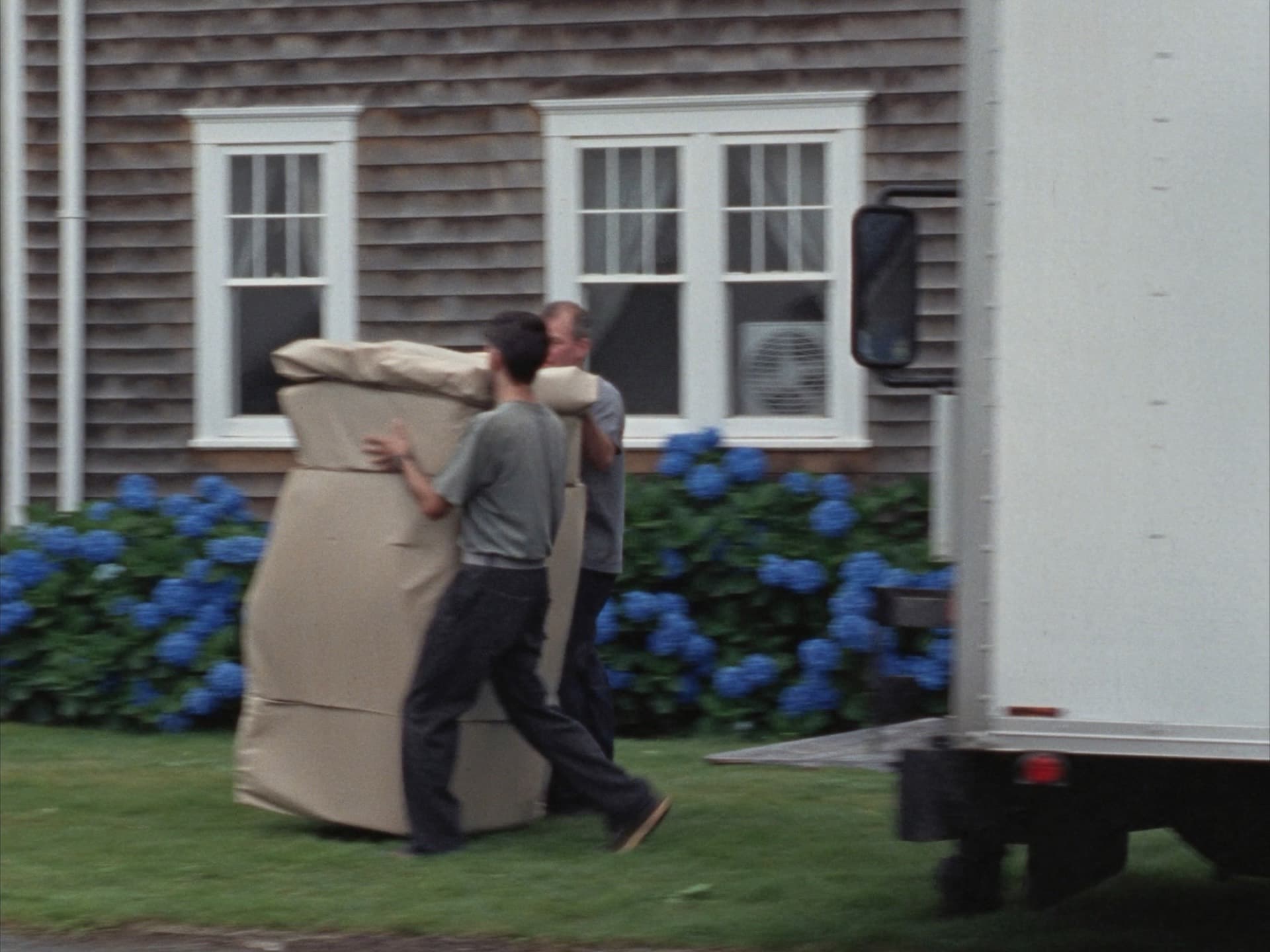 Movers carrying paper-wrapped furniture past hydrangeas